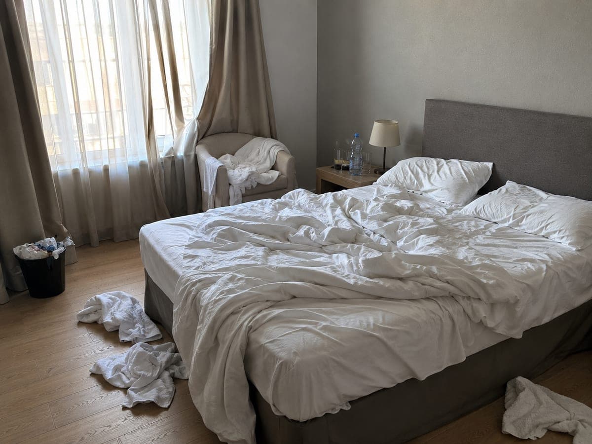 Chambre au lit défait, linge et déchets au sol